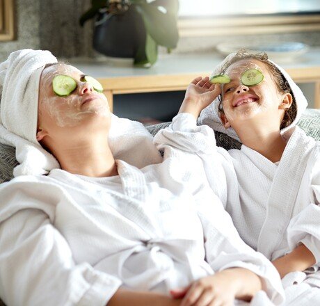 Fresh skincare, face mask and healthy skin treatment for mother and daughter home spa day. Fun, smiling and playful child and single parent relaxing with cucumber over their eyes in grooming routine