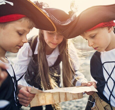 Three little pirates, a girl aged 11 and two boys aged 7 are playing pirates on the beach. They are trying to read ancient treasure map that leads to ... a treasure.