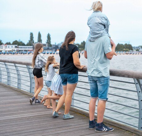 Eine Familie schaut von der Seebrücke über das Meer zur Küste
