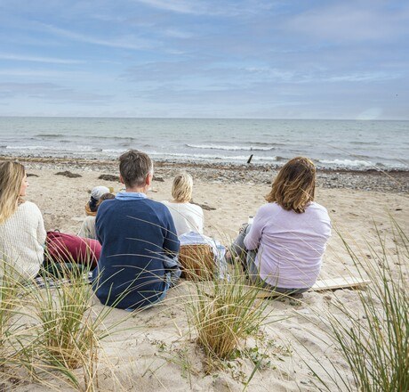 Familie sitzt am Strand und schaut auf das Meer, es ist windig