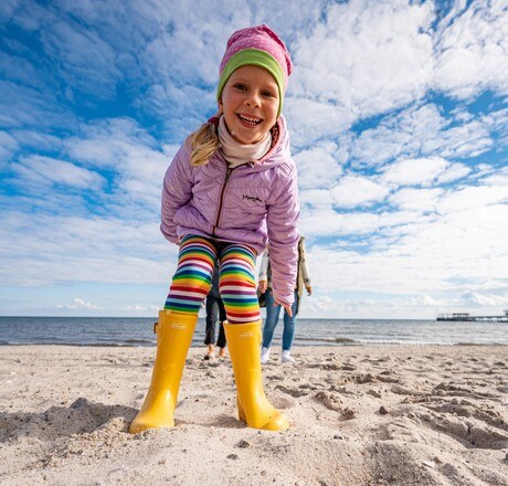 Fröhliches Kind mit gelben Gummistiefeln am Strand