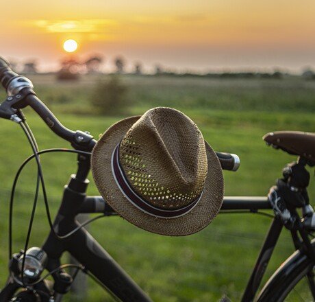 Fahrrad mit einem Hut auf dem Lenker, mit Sonnenuntergang im Hintergrund